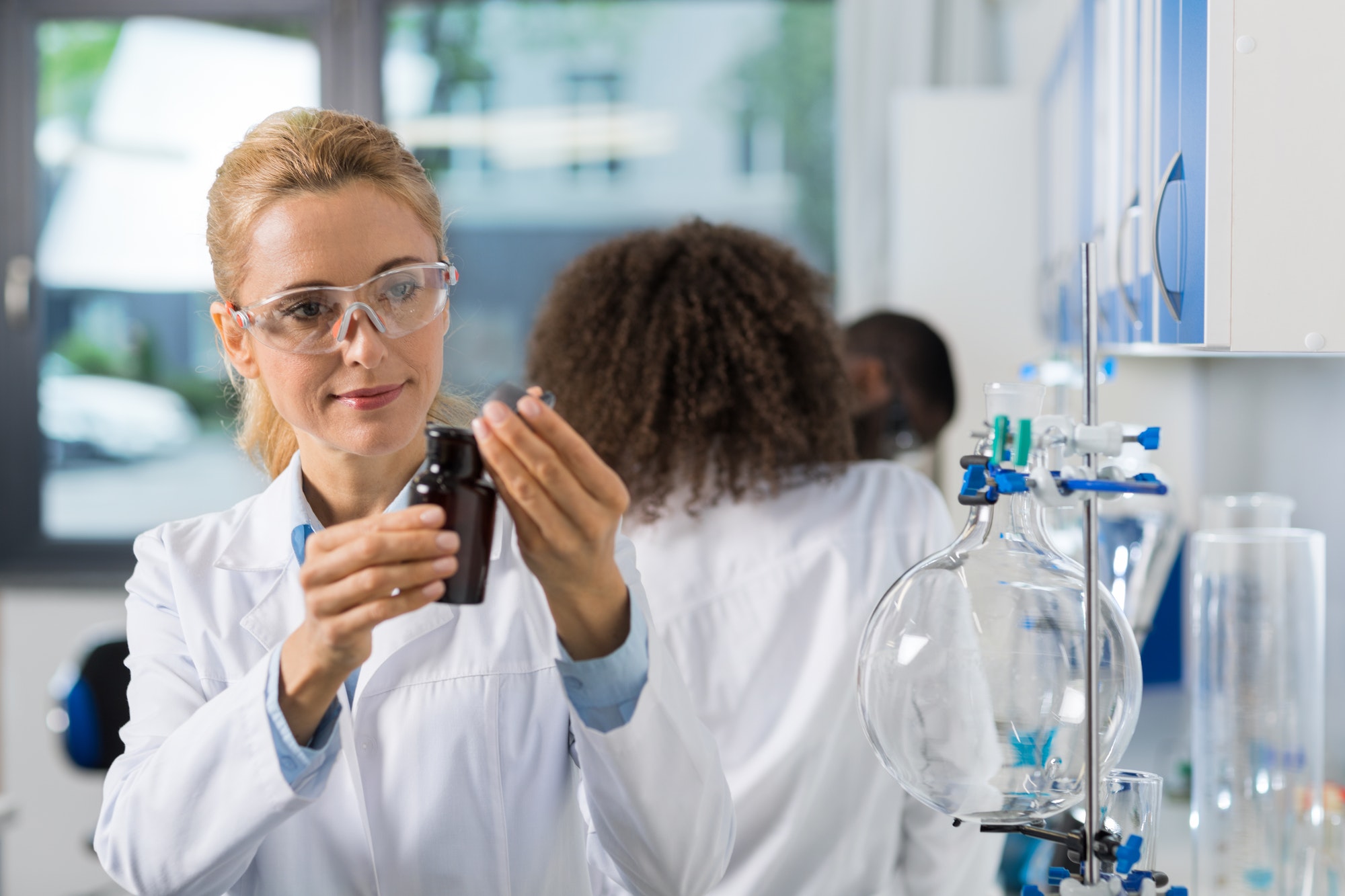 female scientific researcher in laboratory doing research woman working with chemicals over group